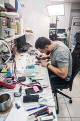 Electronics repair shop, a repairman is surrounded by tools and equipment. A technician repairs,...