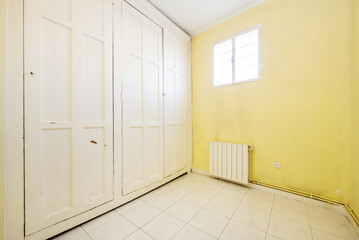 An empty room with walls covered by a large built-in wardrobe with vintage-style white wood doors and yellow painted walls