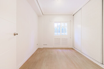 An empty room with walls covered in white cabinets with Venetian style sliding doors and French...