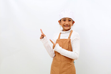 Happy little girl in chef uniform pointing something on blank space. isolated on white background