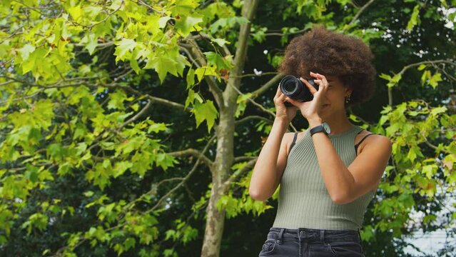 Close up of woman taking photos in city park on DSLR camera viewed from behind - shot in slow motion