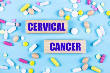 On a light blue background, multi-colored pills and wooden blocks with the text CERVICAL CANCER. Pharmaceutics. Medical concept.