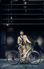 Fototapeta na wymiar Portrait of business man with bicycle standing in front of office building using smartphone.