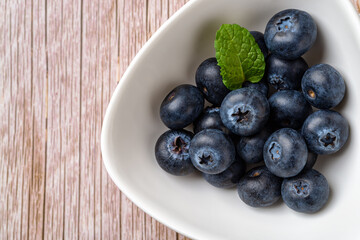 Ripe blueberry in white bowl over wooden surface. Juicy wild berry for vitamin vegan snack. Sweet blueberries vegetarian dessert. Detox diet raw ingredient. Horizontal frame.