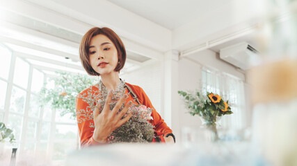 Beautiful Asian Japanese woman florist in apron making bunch of flowers, working in flower shop