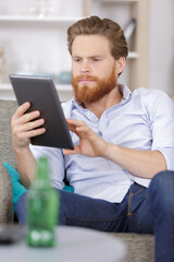 young man with tablet on sofa relaxing at home - obrazy, fototapety, plakaty