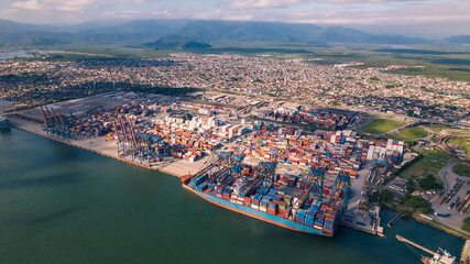 wide drone image of ship docked in port with container terminal and city in the background