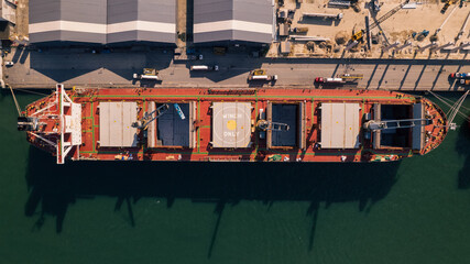 Fototapeta na wymiar Drone image from above of red ship docked in port with cranes loading bulk cargo into the ship's hold