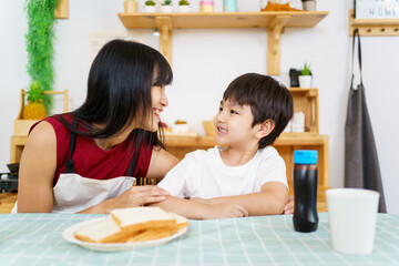 Happy little young boy and his mother making an easy breakfast together in a kitchen with a breads and chocolate jam. Mother and son playing together while making a breakfast.