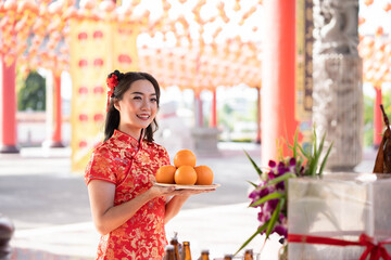 Happy Chinese new year. Beautiful asian woman wearing traditional cheongsam qipao dress holding fresh oranges in Chinese Buddhist temple.