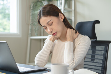 Asian business woman suffering from neck pain working in office sitting at table.