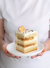 Female hands hold a piece of biscuit cake with cream on a white plate. Festive sweet dessert