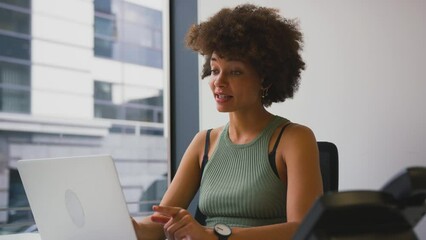 Businesswoman making video call on laptop at desk in modern city office - shot in slow motion - Powered by Adobe