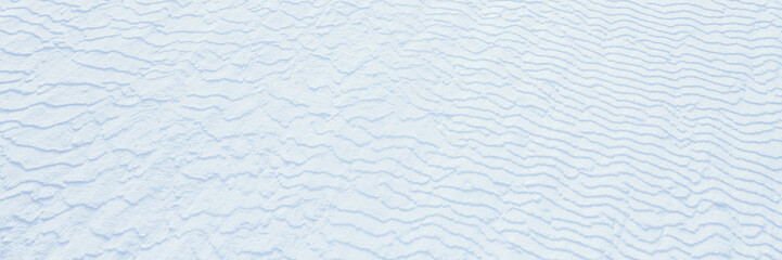 Obraz premium Beautiful winter background with snowy ground. Natural snow texture. Wind sculpted patterns on snow surface. Wide panoramic texture for background and design.
