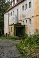 Old residential barrack in the Russian outback. A rickety house, work clay walls, affected by mold and mildew. A dark gloomy entrance with a slate roof. Cracked asphalt, tickets all around