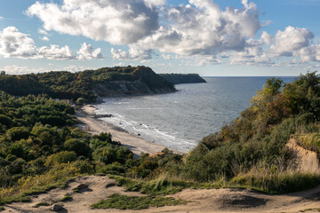View of the Baltic Sea coast from a high cliff. Sandy beach and green forest are below. Steep...