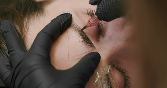 Microblading, permanent makeup tattoo close up. Master makes permanent eyebrow makeup procedure using special needle tattoo machine to woman in beauty salon. Microblading brows tattooing.
