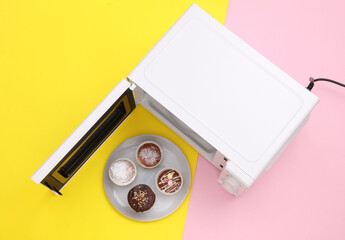 Modern microwave oven with cupcakes on plate, pastel background. food concept. Top view