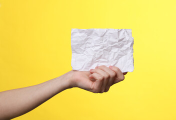 Woman's hand holds empty crumpled white sheet of paper on a yellow background