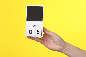 Woman's hand holds wooden calendar with date june 08 on a yellow background