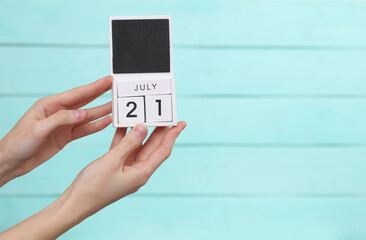 Woman's hand holds wooden calendar with date july 21 on blue wooden background