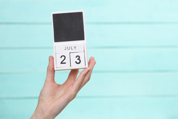 Woman's hand holds wooden calendar with date july 23 on blue wooden background