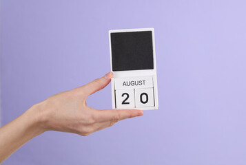 Woman's hand holds wooden calendar with date august 20 on pastel purple background