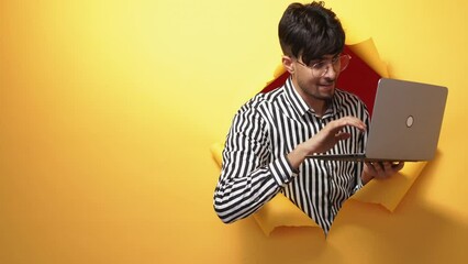 Digital people. Electronic nerd. Information technology. Happy geek man enjoying using laptop in orange breakthrough torn paper hole copy space background.