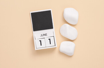 White wooden calendar with the date june 11 on beige background with white pebbles