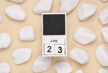 White wooden calendar with the date june 23 on beige background with white pebbles