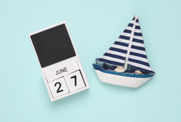White wooden calendar with the date june 27 and sailboat on a blue background. Travel concept. Top view
