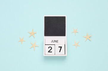 White wooden calendar with the date june 27 and sea stars on a blue background. Summer time. Top view