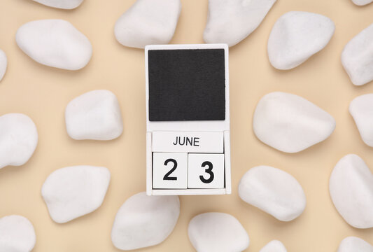 White wooden calendar with the date june 23 on beige background with white pebbles