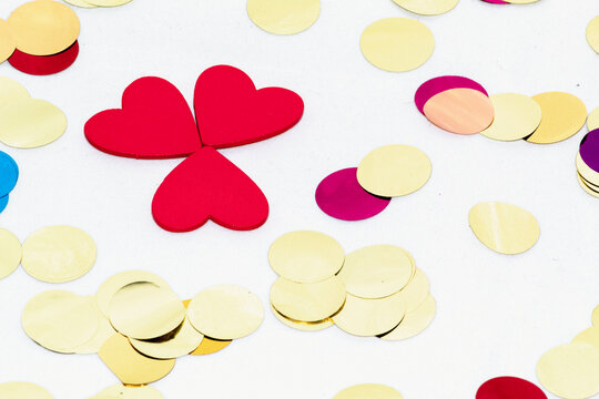 Fondo blanco con confeti de colores por todos lados y tres corazones rojos de madera a un lado haciendo la forma de trevol.