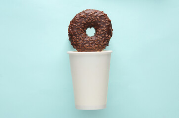 Cardboard cup with chocolate donut on blue background