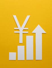 Fototapeta premium Paper-cut columns of a chart tending upwards and yuan symbol on yellow background. Analytics, business concept