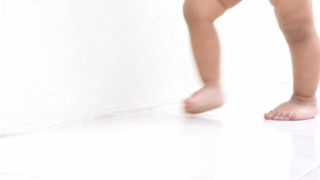 close-up of a brunette baby's feet, learning to walk on a white tiled floor