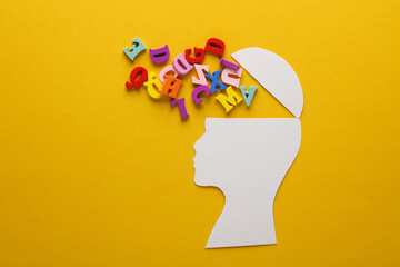 Paper-cut open human head with letters on yellow background. Mental health, education, open mind...