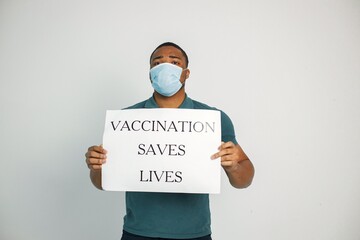 Black guy in face mask holding a poster with words vaccination saves lives