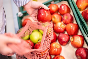Picking the right apple in the market. Unrecognizable woman with a reusable cotton bag buying apples in the grocery store.
