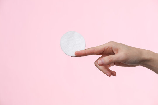 White cotton hygienic disc in a female hand on a pink background