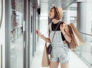 Young stylish woman with shopping packages looks into a shop window in a mall. Shopping concept