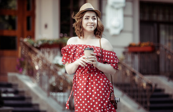 Beautiful women in red polka dot dress and hat holding coffee cup in the city