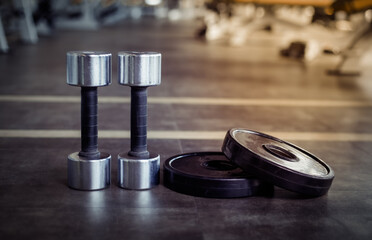 Metal dumbbells and barbell discs on gym floor. Fitness, bodybuilding and functional training...