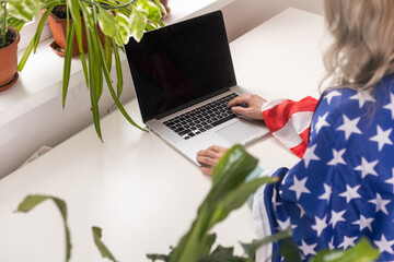 Happy woman employee sitting wrapped in USA flag, shouting for joy in office workplace, celebrating labor day or US Independence day.