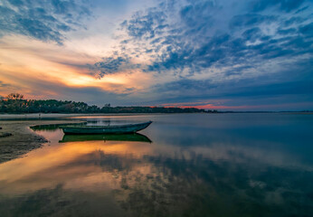 Lonely boat on the river at sunset. Picturesque clouds reflected in calm water