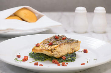 Grilled fish and spinach on a white plate with bread