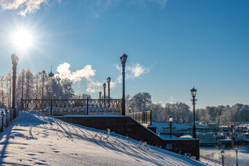 Fototapeta na wymiar City embankment covered with snow and covered with hoarfrost in severe frost in sunny weather in winter.