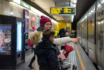 A Caucasian woman with her teenage son in a subway station, pointing to the wagon to board. 