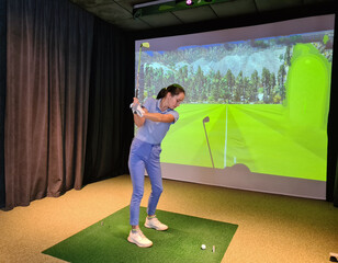 Beautiful female golfer makes a swing golf club indoors